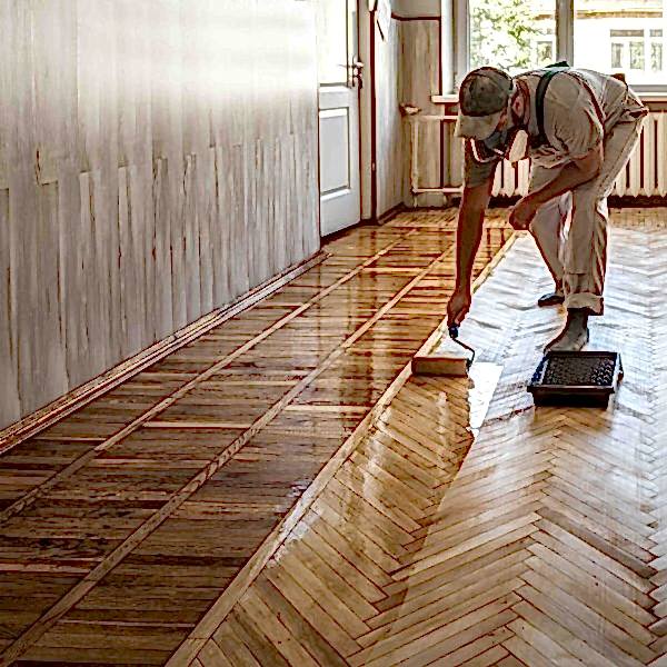 Flooring professional applying finish to a herringbone parquet hardwood floor in an older home.