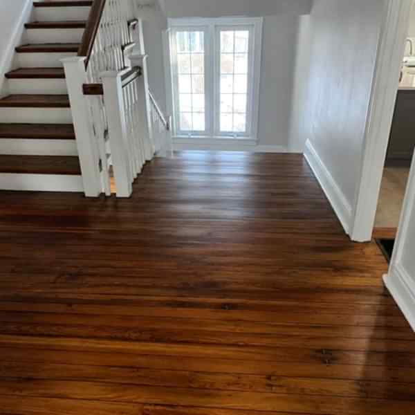 Refinished dark hardwood floors in an empty property living room with staircase and natural light
