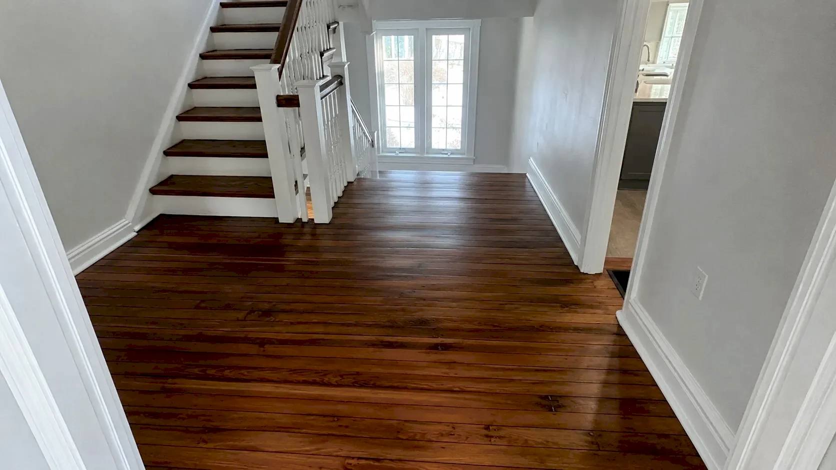 Refinished dark hardwood floors in an empty property living room with staircase and natural light