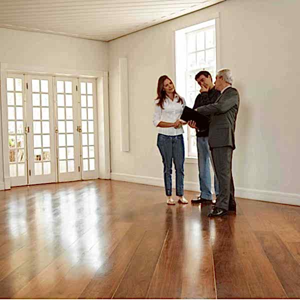 Homebuyers and real estate agent evaluating hardwood floors during a home showing.
