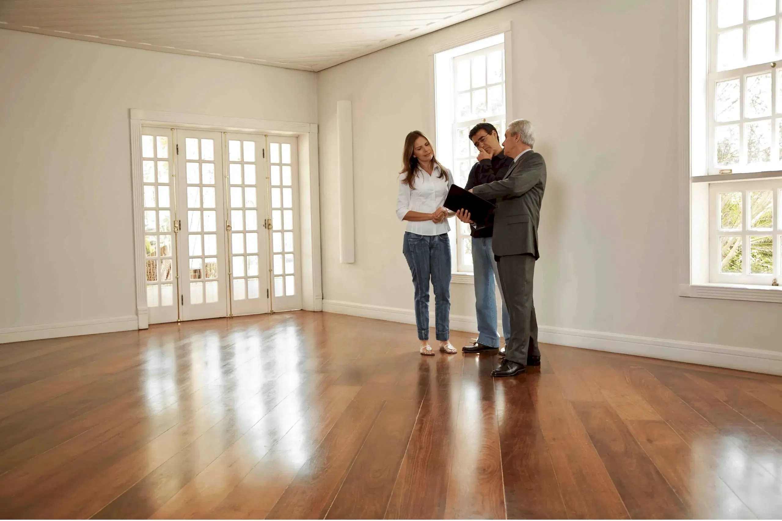 Homebuyers and real estate agent evaluating hardwood floors during a home showing.